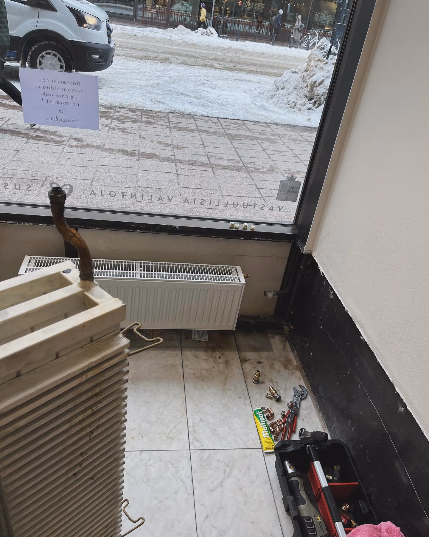 Vanha patteri on irrotettu ja uusi lämmityspatteri asennettu ikkunan alle, putkityökalut lattialla.